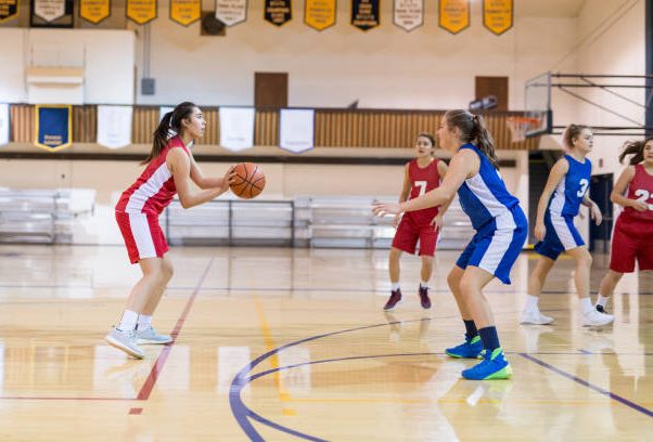 An ethnic female player spots up to shoot a three-pointer from the top of the key. Her opponent is guarding her loosely.
